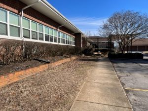 The side of a school with a sidewalk leading to the entrance.