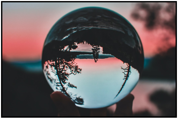 A glass ball being held up to a sunset and trees reflecting it upside down.