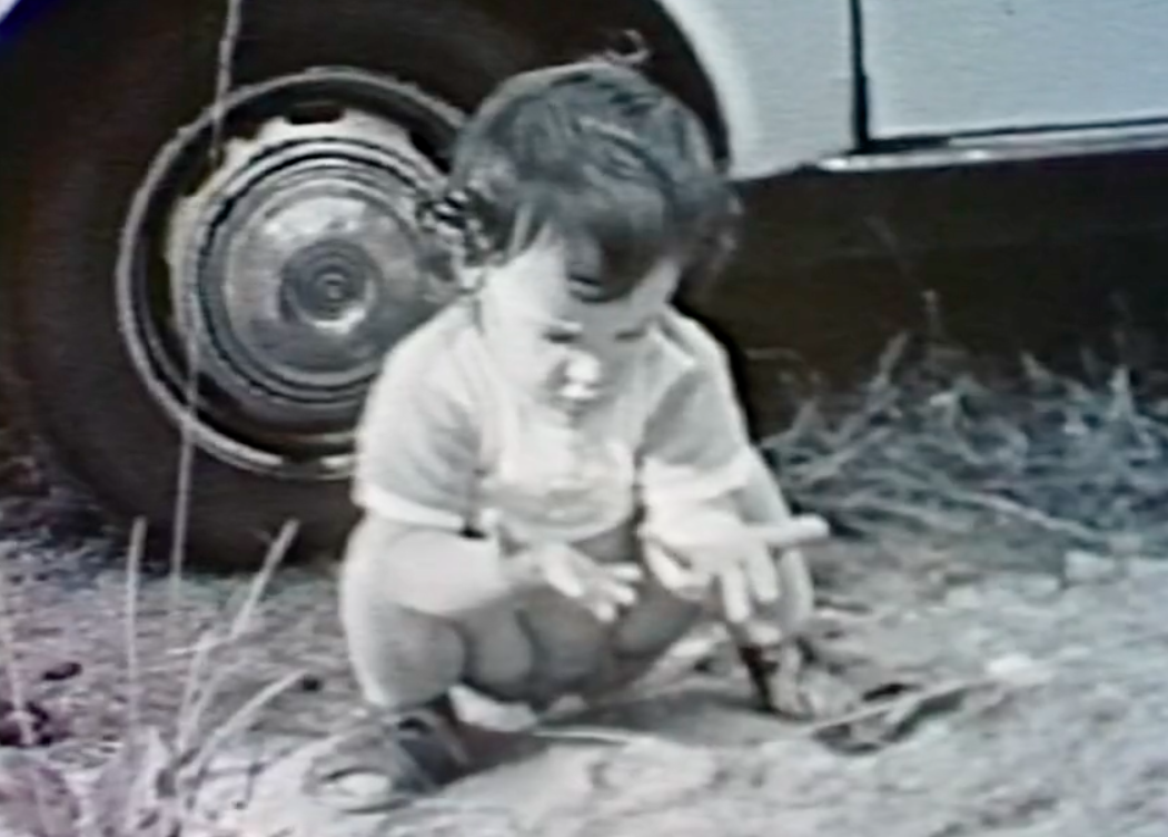 A black-and-white childhood photo of the author as she squats and stares at her outstretched hands.