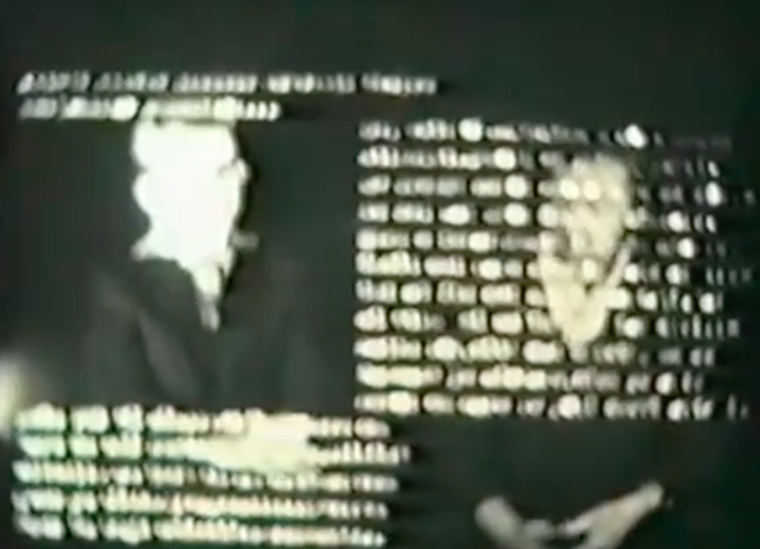 A blurry film still in which two men sit side by side. The top half of the man on the right is obstructed by illegible text and the bottom half of the man on the left is obstructed by illegible text.