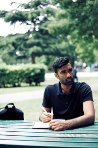 A man sitting at a table, with a notepad and pen, thinking intently.